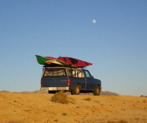 Desert Road with blue truck with kayaks on roof.